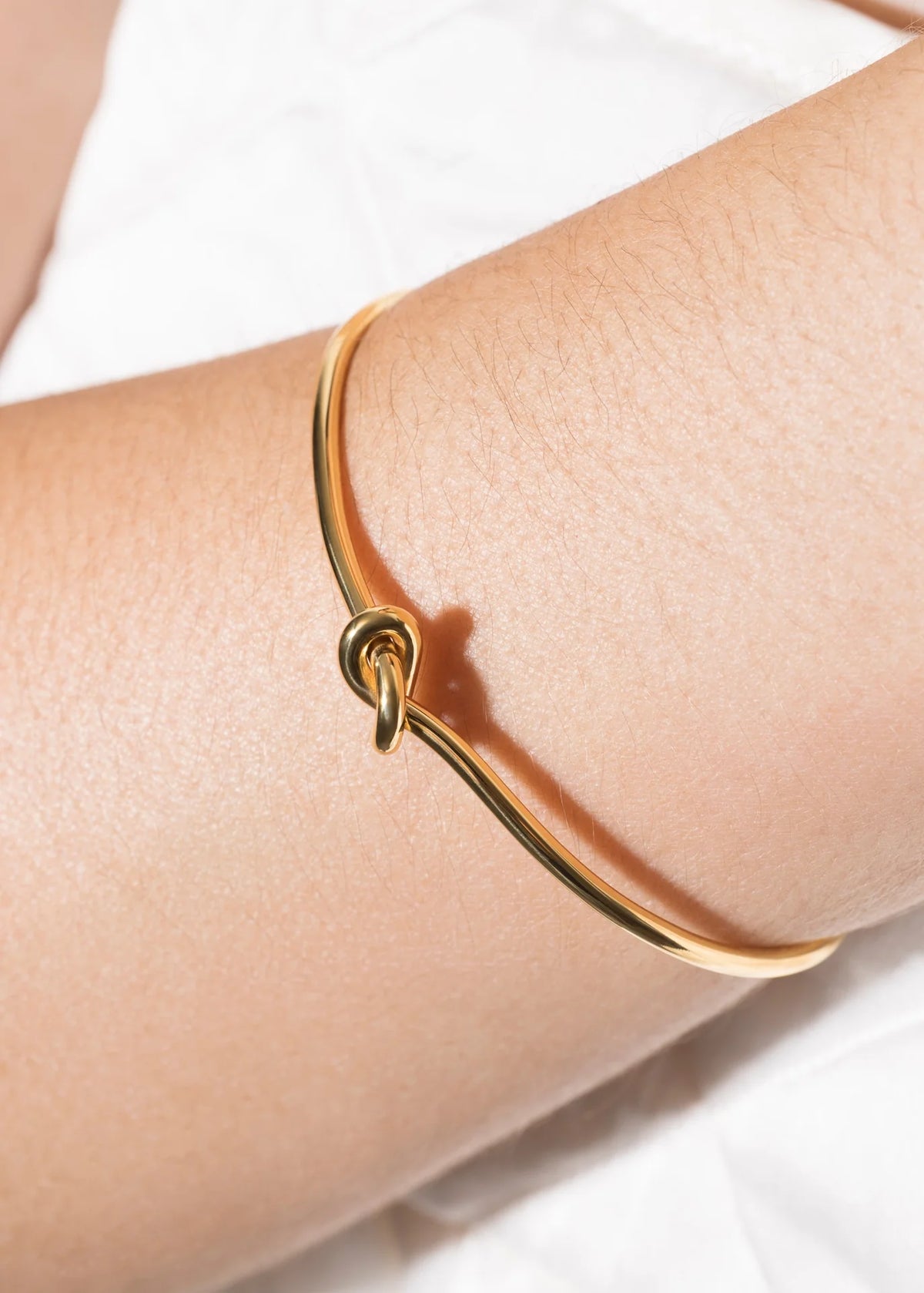 Delicate layered bracelet styling featuring a minimalist gold bracelet with a knot detail, elegantly worn on an arm.
