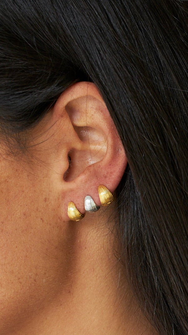 Gros plan d'une oreille portant des boucles d'oreilles en or sur un fond neutre