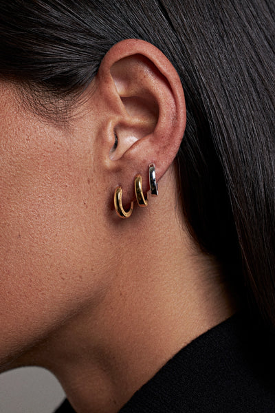 Close-up of a person's ear wearing three small hoop earrings in gold, silver, and black.