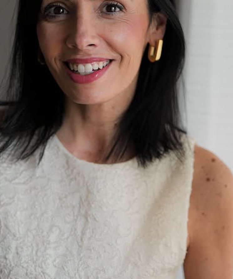 Sorriso de mulher com blusa clara e brincos dourados, usando joias da CINCO.