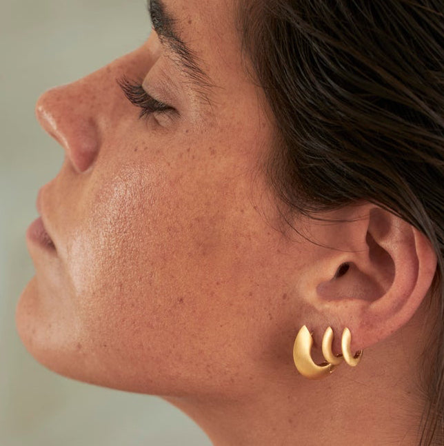 Woman with wet hair wearing gold earrings in a bathroom setting