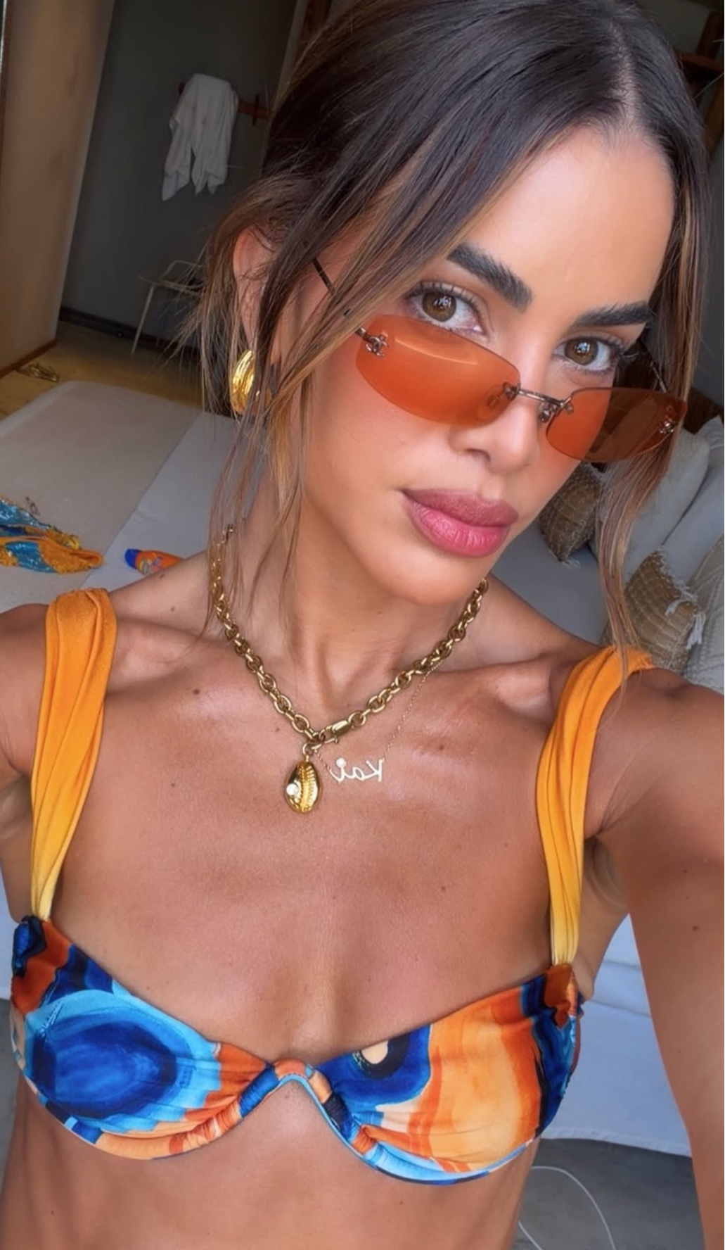 Woman wearing a colorful bikini and orange sunglasses indoors.