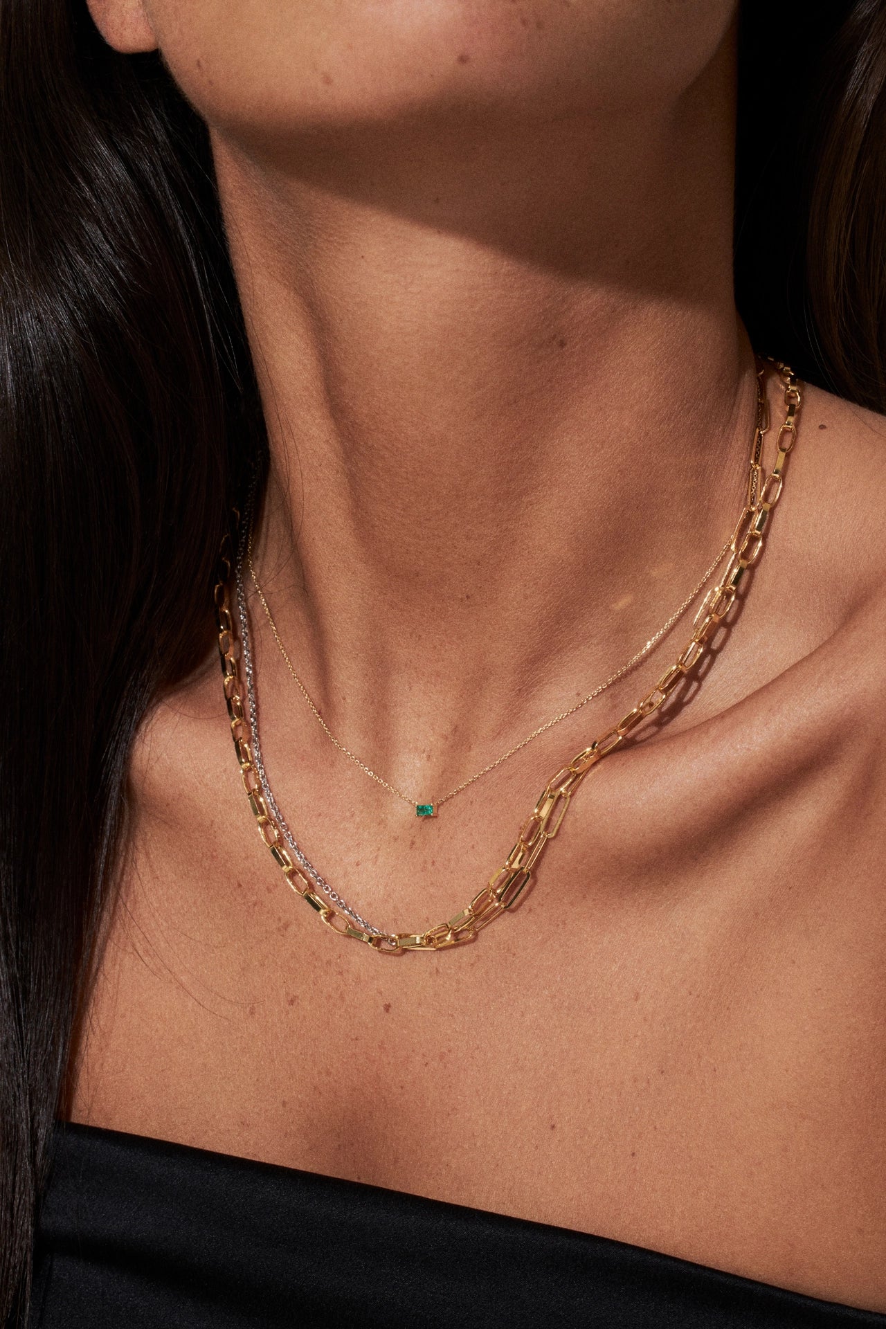 Close-up of a person wearing a gold chain necklace with a small green gemstone.