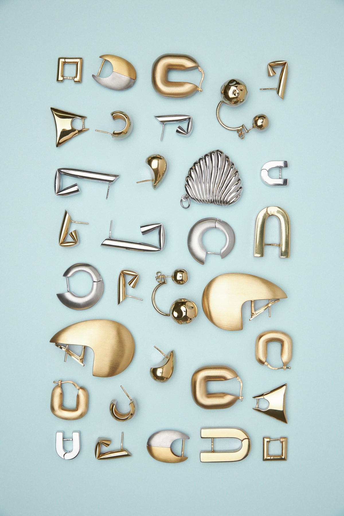 A collection of gold and silver geometric earrings arranged in a grid on a light blue background.