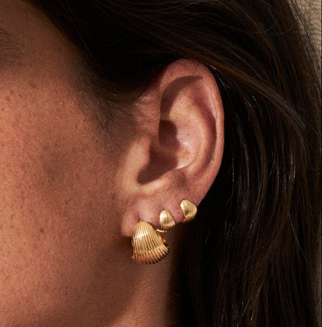Close-up of a woman wearing gold earrings with a neutral background