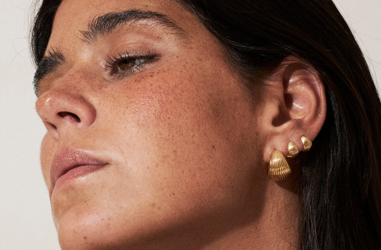 Close-up of a woman wearing gold earrings against a neutral background
