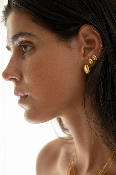 Gros plan d'une femme portant des boucles d'oreilles en or sur un fond neutre