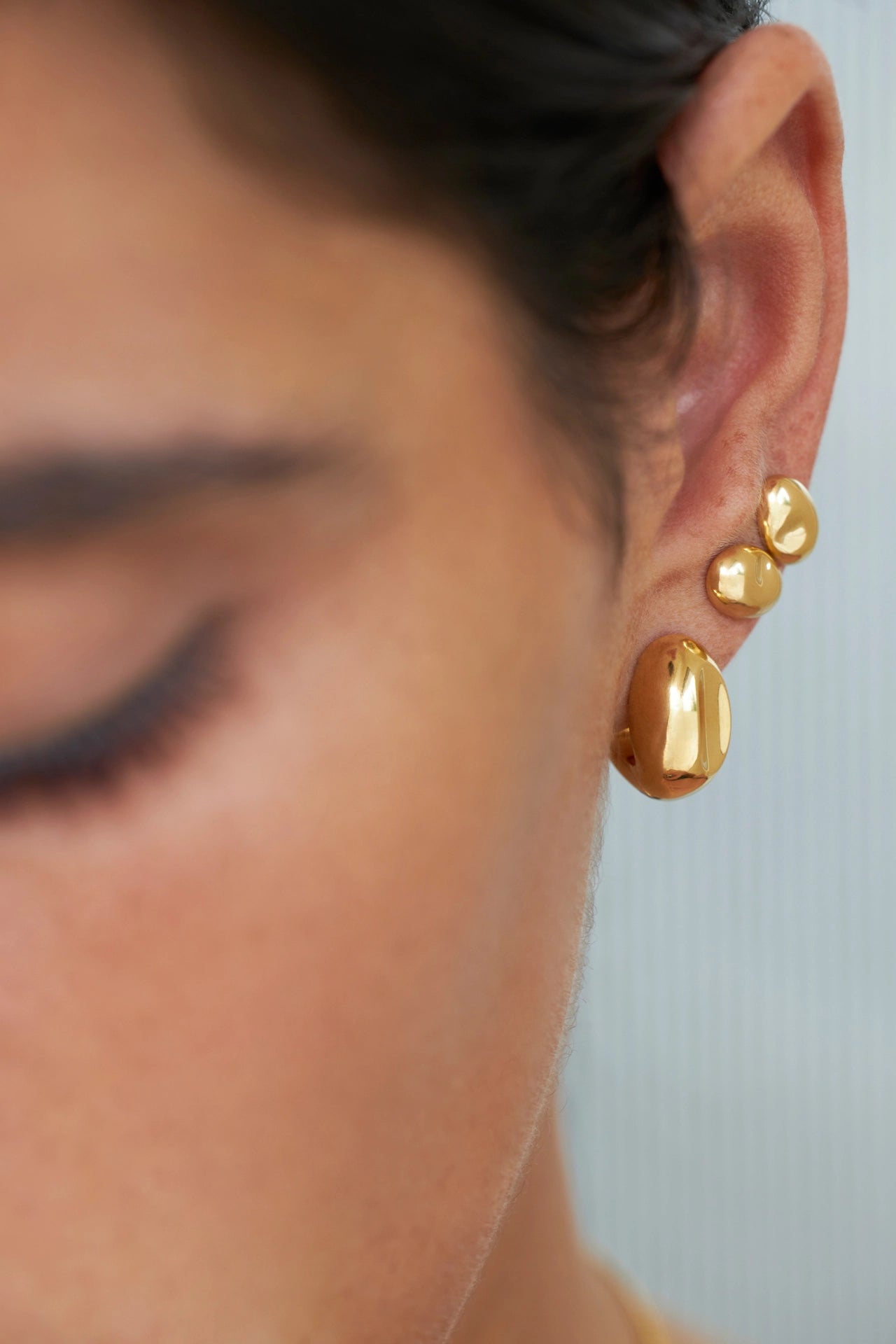 Gros plan d'une personne portant des boucles d'oreilles en or sur un fond neutre